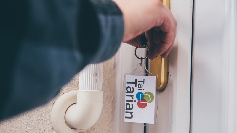 A tenant unlocking a door with a key on a Tai Tarian keyring