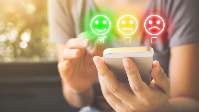 A person uses a mobile phone to submit feedback. They have three options to choose from - happy, neutral and sad - indicated by graphics of facial expressions.