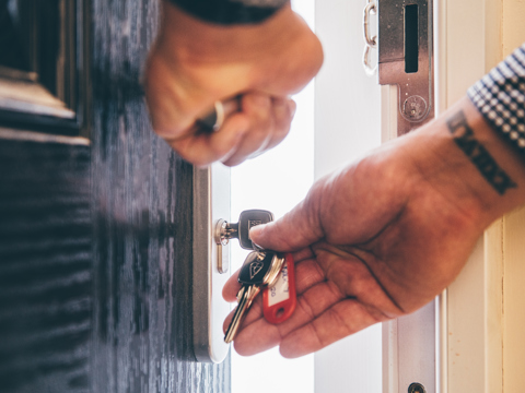 Close-up of a person unlocking a front door with a key, holding a set of keys in their hand.